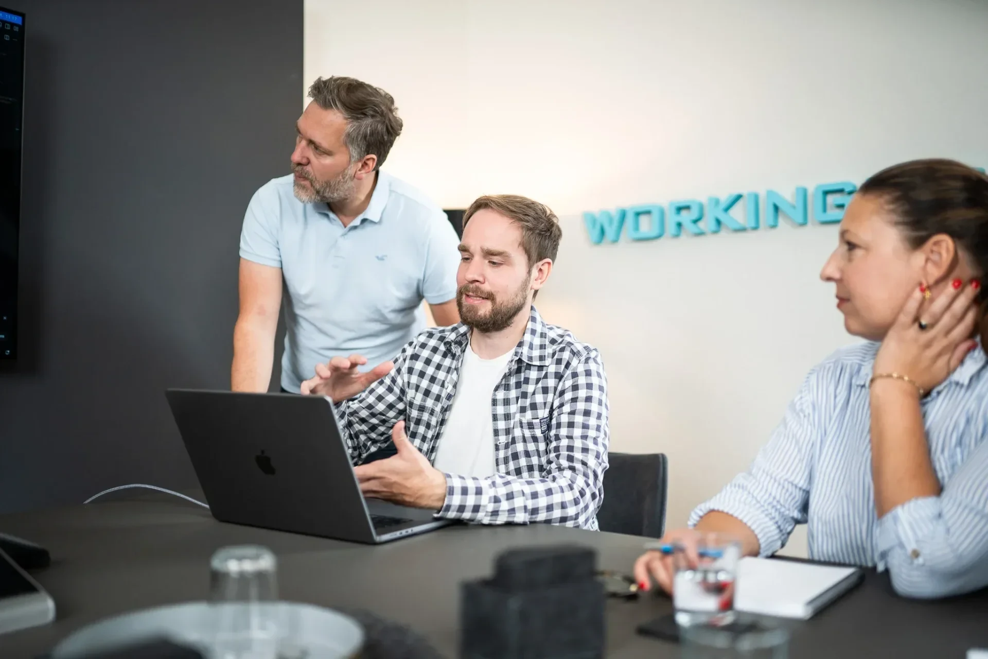 Zwei Männer und eine Frau besprechen etwas an einem Notebook, an der Wand der Schriftzug workingbits.